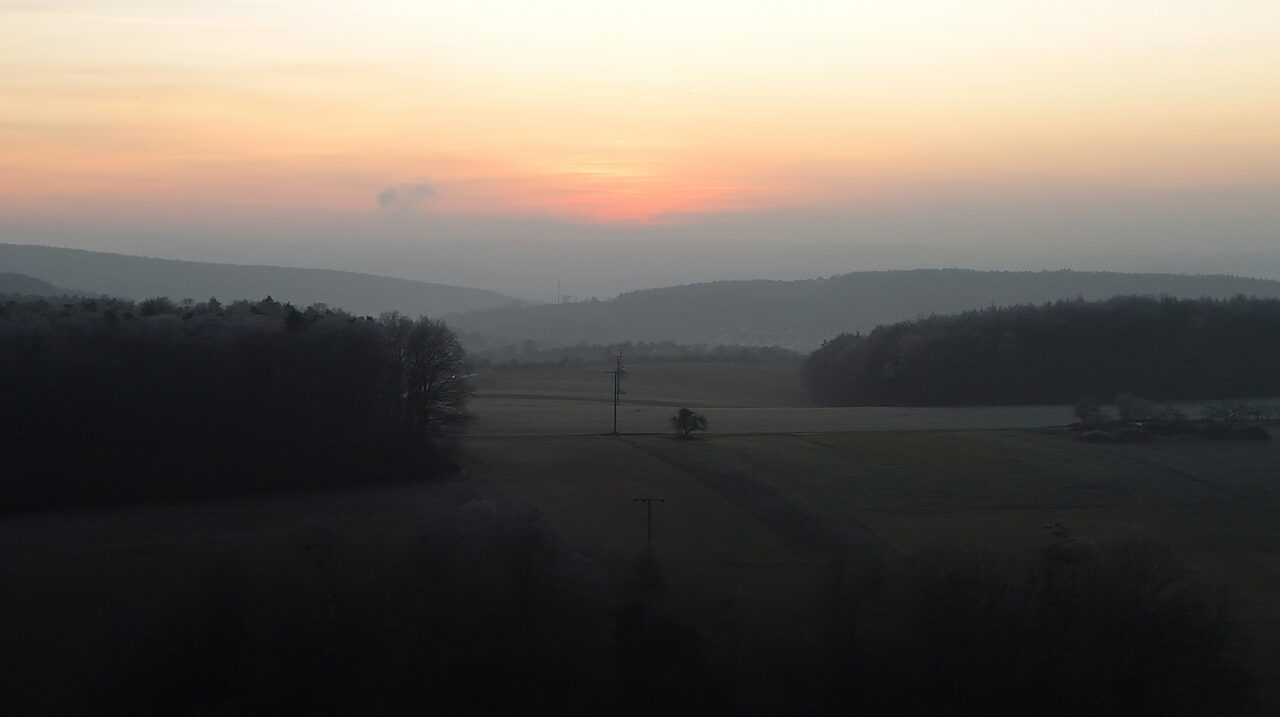 Weite Hügellandschaft mit Wäldern im letzten Abendlicht
