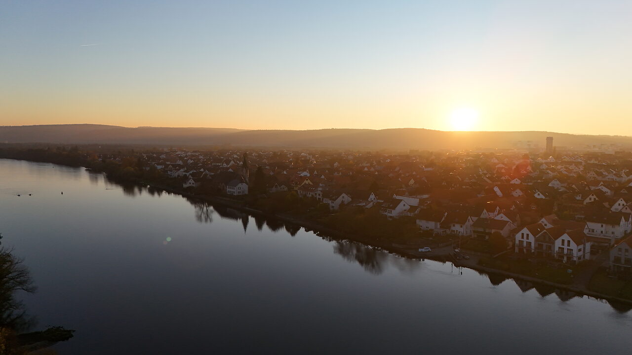 Sonnenuntergang über einem Fluss mit Ortschaft am Ufer