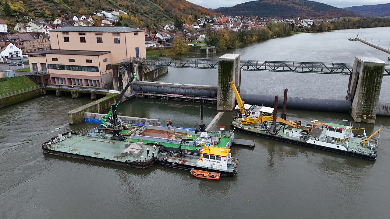 Luftaufnahme einer Staustufe mit Arbeitsschiffen und Baustelleneinrichtung auf dem Fluss