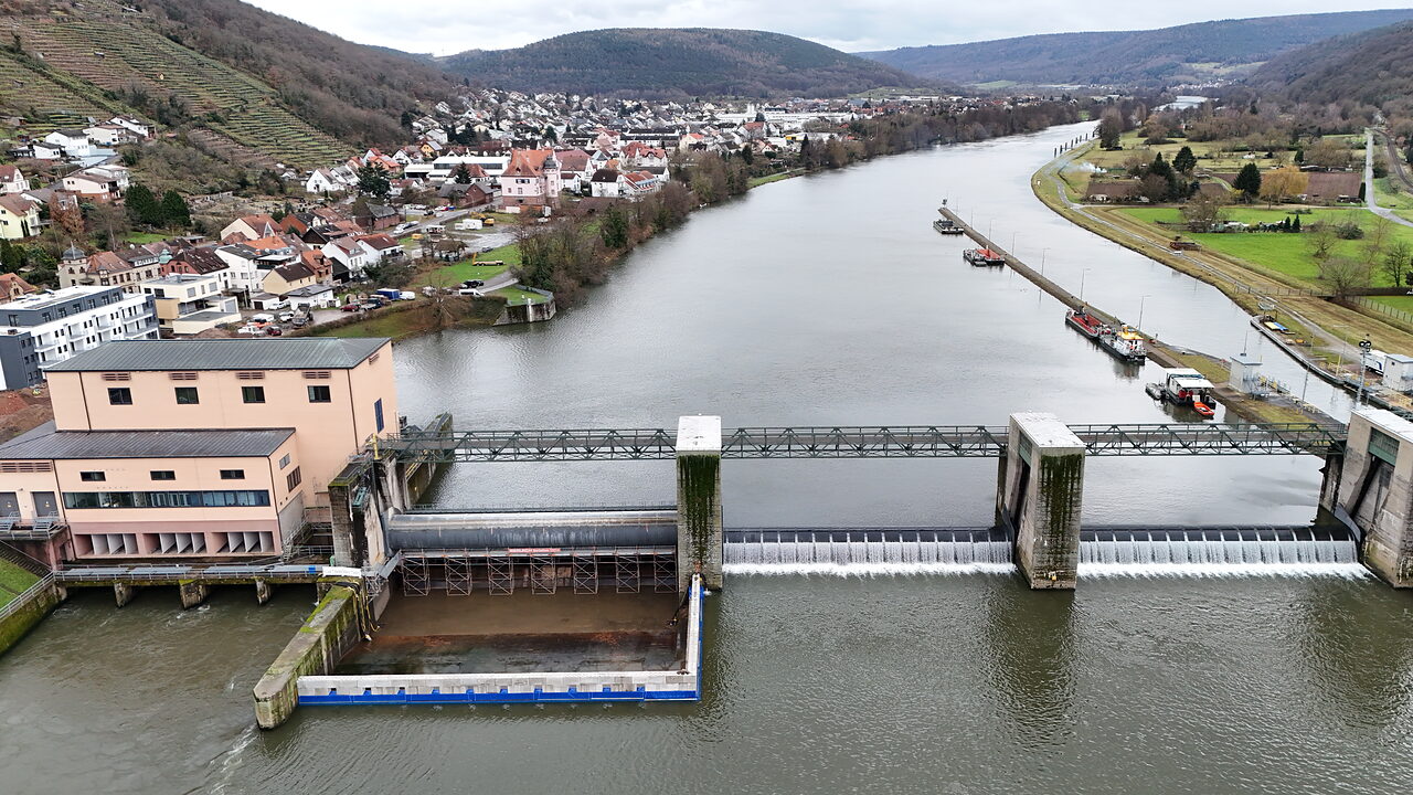 Wehranlage im Fluss mit Ortschaft und Hügellandschaft